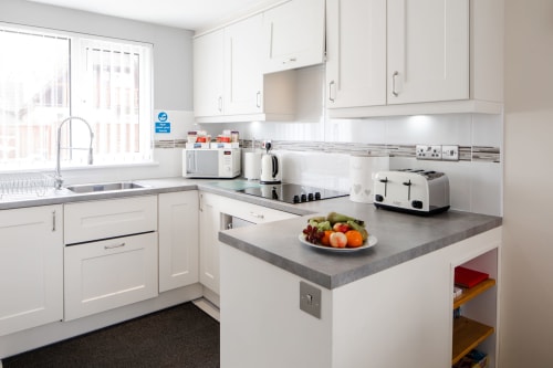 Cornish Holiday - 100 Hengar Manor. Kitchen area with microwave, kettle, ceramic electric hob, 4 slice toaster, dishwasher, fan assisted oven, lots of cupboards and a plate of fruit.