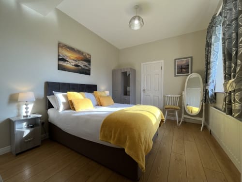 Room 6 at Steeple View B&B in Donegal featuring black bed with yellow bedding, cream walls, wooden floors and ensuite