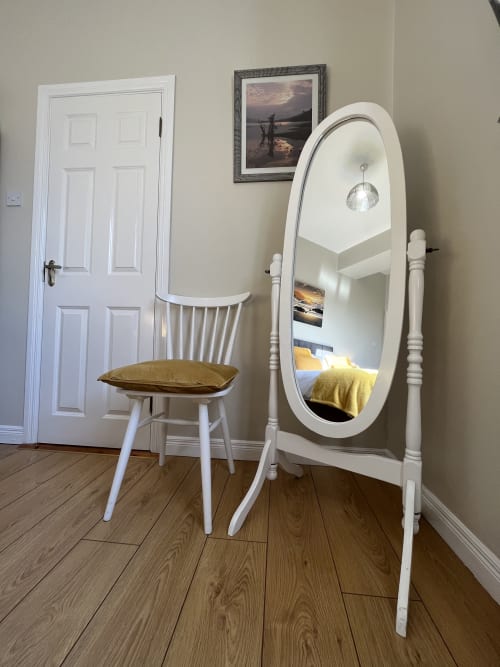 Room 6 at Steeple View B&B features a white framed mirror, wooden chair with gold cushion, and coastal artwork on beige