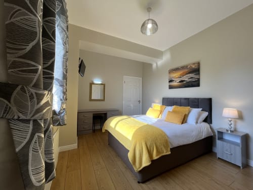 Modern bedroom at Steeple View B&B in Donegal with grey bed, yellow accents, wooden floors, and ensuite facilities