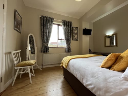 Modern bedroom at Steeple View B&B Donegal with double bed, white chair, flat-screen TV, and gray curtains overlooking