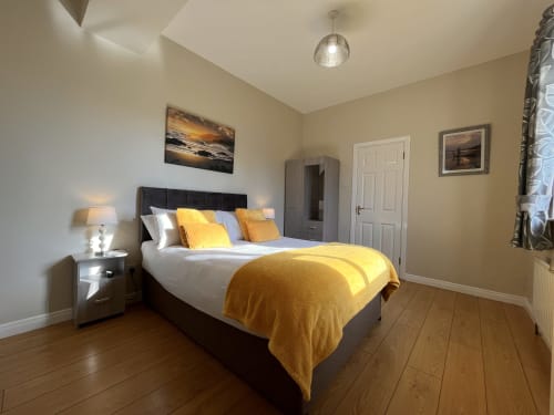 Bright bedroom at Steeple View B&B in Donegal with yellow bedding, dark headboard, ensuite door, and wooden flooring