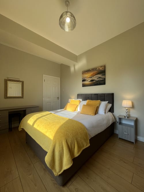 Room 6 at Steeple View B&B Donegal with yellow accents, black bed, grey nightstand, pendant light, and landscape artwork.