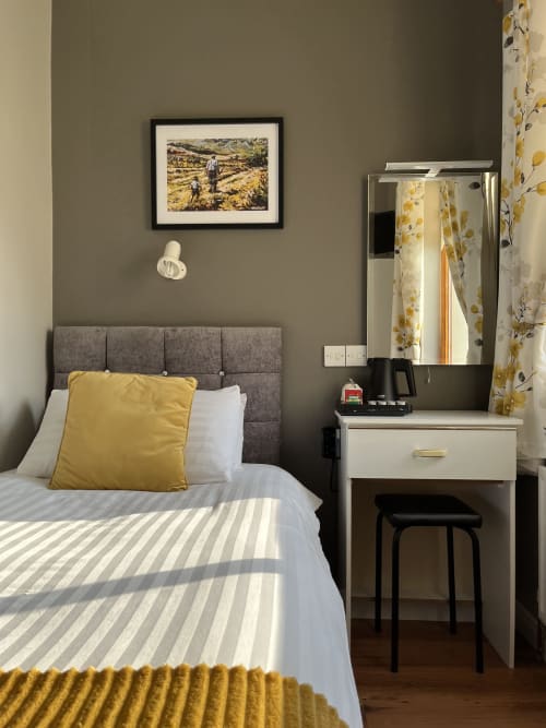 Modern bedroom at Steeple View B&B in Donegal with gray upholstered bed, yellow accents, vanity desk with mirror, and framed