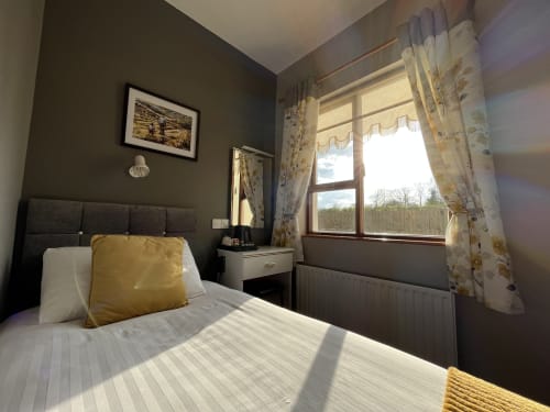 Bright bedroom at Steeple View B&B Donegal with dark grey walls, yellow accent pillow, and countryside views through large