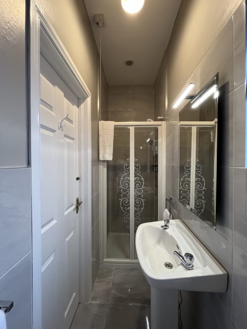 Modern private ensuite bathroom at Steeple View B&B Donegal with walk-in shower, pedestal sink, and tiled walls