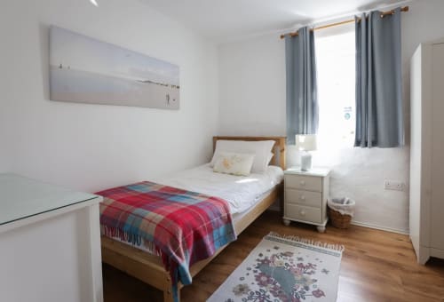 Bright bedroom in The Barn cottage at Ballymultimber, Limavady, with wood bed, plaid throw, blue curtains, and mountain view