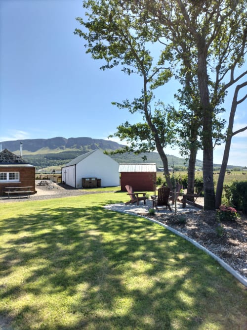 Ballymultimber Cottages barn with mountain views, green lawn, and seating area under trees in Limavady