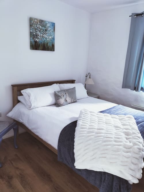 Bright bedroom in The Barn cottage at Ballymultimber with wooden bed, white linens, and mountain view artwork at Limavady.