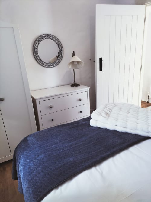 Modern bedroom in The Barn cottage at Ballymultimber, Limavady, with white dresser, decorative mirror, and navy bedding
