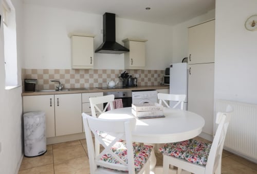Bright kitchen-diner with cream cabinets, checkered backsplash, black range hood, round white dining table with floral chair