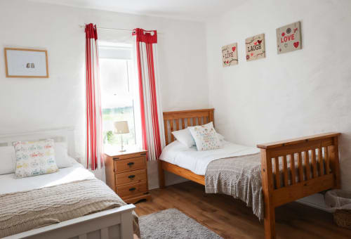 Bright children's bedroom in The Garden cottage at Ballymultimber, Limavady with twin wooden beds and red curtains