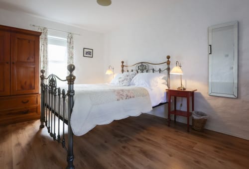 Bright bedroom with black metal bed frame, wooden furniture, and hardwood floors at Ballymultimber Cottages, Limavady