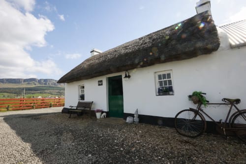 Cissy's Cottage at Ballymultimber, Limavady with thatched roof, white walls, green door, and mountain views in background