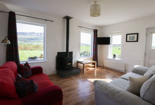Spacious living room at Ballymultimber Cottages with red sofa, wood stove, and countryside views in Limavady