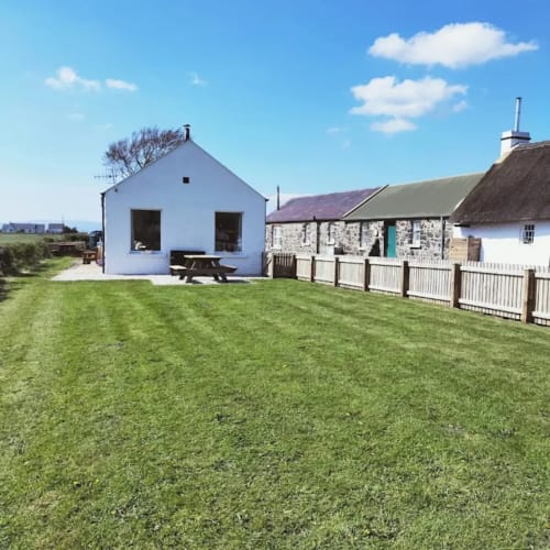 Ballymultimber Cottages garden cottage in Limavady with green lawn and traditional stone buildings