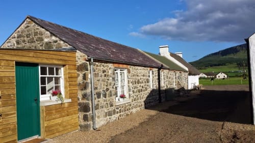 Stone cottage at Ballymultimber Cottages in Limavady with green door, mountain views, and gravel courtyard