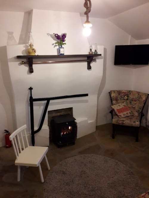 Cozy sitting area at Cissy's Cottage in Limavady with fireplace, armchair, and wall-mounted shelving