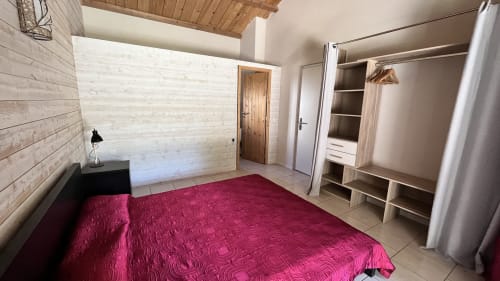 Chambre spacieuse de la villa Le Maquis Plage avec lit bordeaux, mur en bois et armoire intégrée