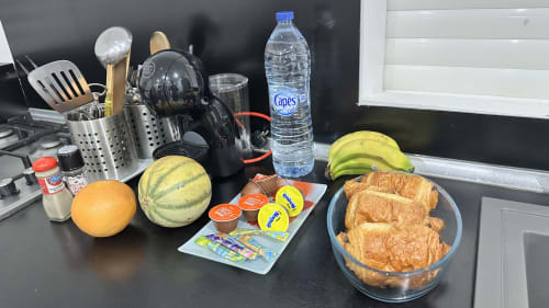 Petit-déjeuner Kaz A Bibi Sainte-Rose avec fruits frais, viennoiseries, eau et ustensiles de cuisine sur le plan de travail