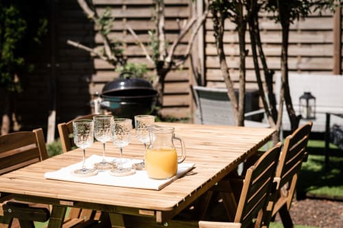 Outdoor wooden dining table at Villa Eden Bleu in Biscarrosse with glasses, orange juice pitcher, and garden setting