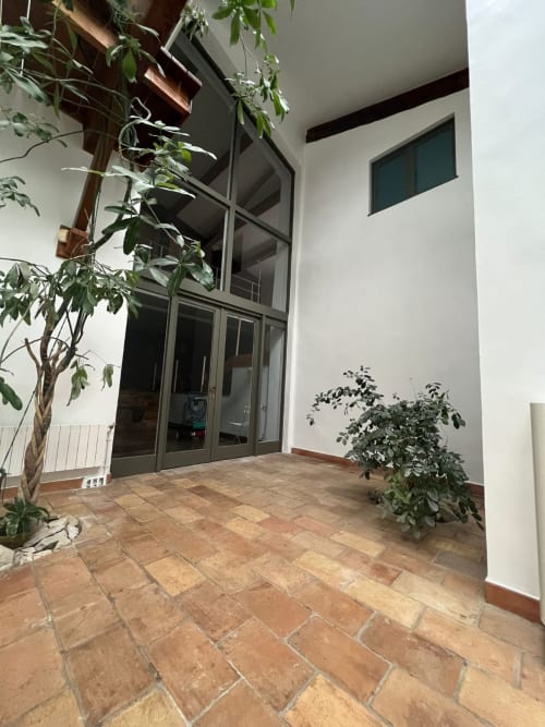Covered terrace with terra cotta tile flooring, potted plants, and glass doors at La Conciergerie De Franck villa in