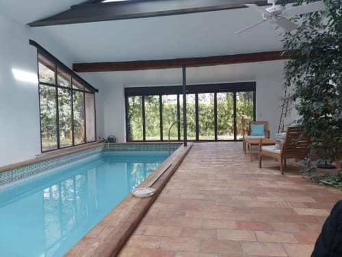 Indoor swimming pool with large windows overlooking gardens at La Conciergerie De Franck villa in Boissieres