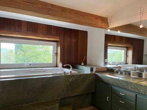 Luxury bathroom with dark marble vanity, wooden beams, large windows overlooking gardens at La Conciergerie De Franck villa