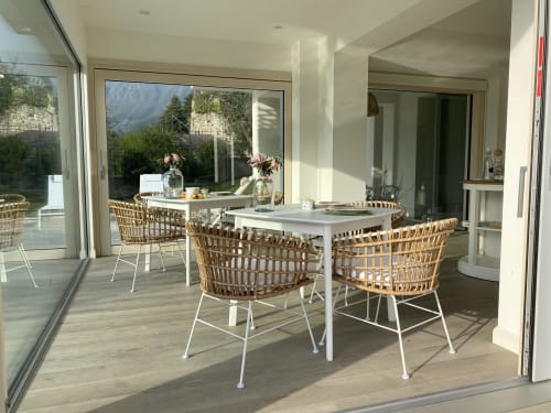 Zona pranzo moderna all'aperto presso Verdolivo B&B a Sale Marasino con sedie in vimini, tavoli bianchi e vista sulle montagne