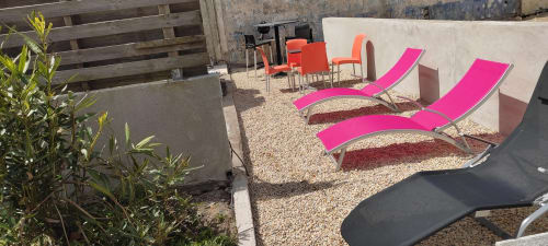 Chaises longues roses sur patio en gravier à la Résidence des dunes, Landéda, avec murs blancs et terrasse en bois
