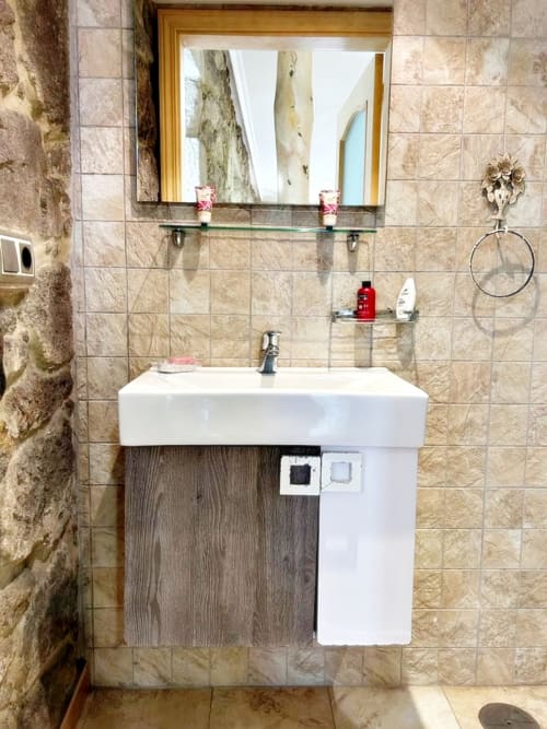 Baño moderno en apartamento de Baiona con lavamanos blanco, paredes de azulejos beige, espejo enmarcado y estantes de vidrio