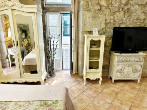 Elegante dormitorio en loft Peperete, Baiona con muebles crema, muros de piedra, TV y vistas a la ciudad