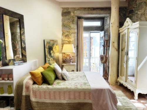 Dormitorio luminoso con cojines verdes y dorados, paredes de piedra y vistas a balcón en loft de Baiona
