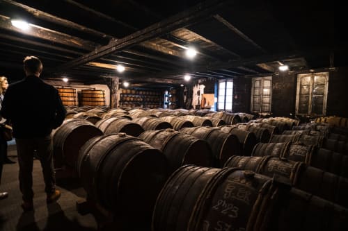 Cellier de barriques à la maison de cognac Logis des Tourelles en France, avec des visiteurs explorant des tonneaux de chêne vieillis