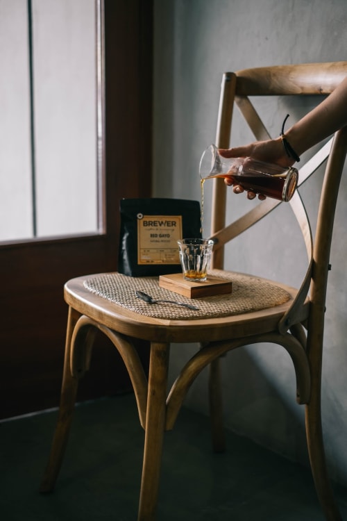 Personne versant un café Brewer à Logis des Tourelles, gîte de charme en Cognac, avec chaise en bois et verre