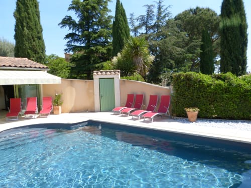 Funkelnder Pool mit roten Liegen in der Villa Thébaïde, Laudun L'Ardoise, umgeben von üppigen Gärten