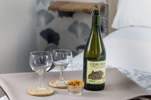 Bouteille de cidre Bouché avec deux verres de vin et des amuse-bouches sur table en chambre de l'Hôtel De Lion Sur Mer