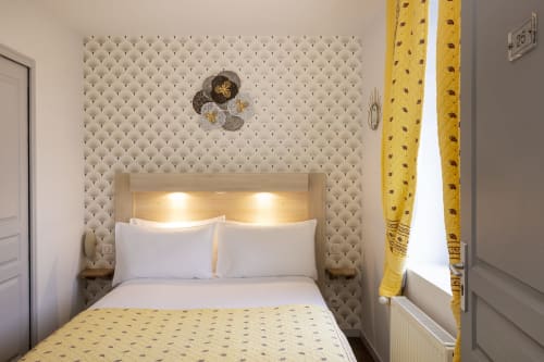 Chambre double confortable à l'Hôtel De Lion Sur Mer avec tête de lit capitonnée beige, rideaux jaunes et éclairage moderne