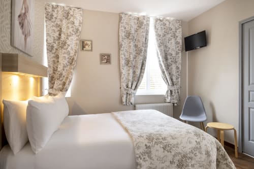 Chambre double Confort à l'Hôtel De Lion Sur Mer avec literie blanche, rideaux fleuris, TV écran plat et équipements modernes