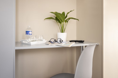 Bureau minimaliste dans la chambre double confort de l'Hôtel De Lion Sur Mer avec plante en pot, bouteille d'eau, verres et fournitures de bureau