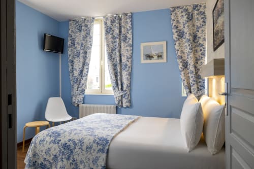Chambre double confortable à l'Hôtel De Lion Sur Mer avec murs bleus, rideaux à fleurs, TV écran plat et équipements modernes