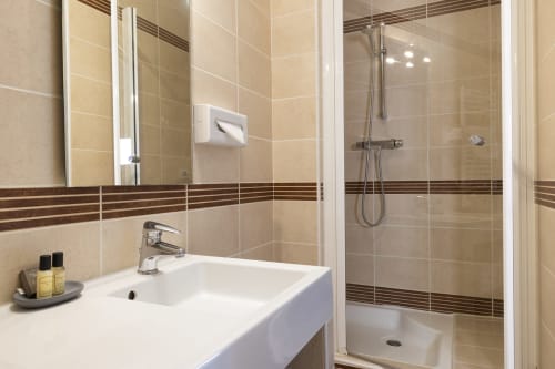 Salle de bains moderne dans la chambre Comfort Double de l'Hôtel De Lion Sur Mer avec lavabo blanc, miroir et douche à l'italienne fermée