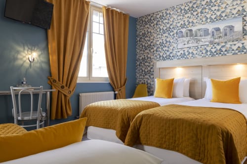 Chambre triple moderne à l'Hôtel De Lion Sur Mer avec lits jumeaux, literie dorée, papier peint bleu motifs et vue sur la ville
