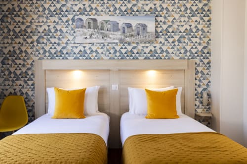Lits jumeaux aux accents jaunes dans une chambre moderne de l'Hôtel De Lion Sur Mer, Lion sur Mer, avec papier peint géométrique