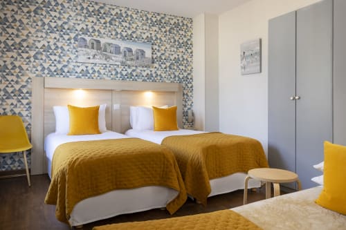 Chambre triple moderne à l'Hôtel De Lion Sur Mer avec lits jumeaux, parure dorée, papier peint géométrique et vue sur la ville