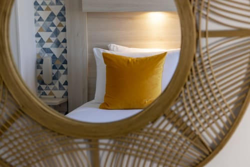 Chambre d'hôtel moderne à l'Hôtel De Lion Sur Mer avec oreiller jaune sur le lit, art mural géométrique et détails de chaise tressée