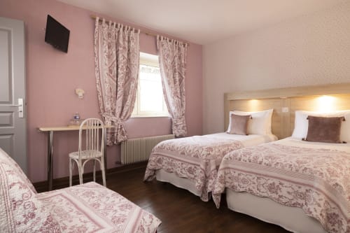 Chambre triple de l'Hôtel De Lion Sur Mer avec murs roses, lits jumeaux, bureau, fenêtre avec rideaux et télévision écran plat