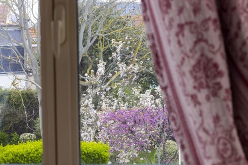 Vue du jardin de printemps depuis la chambre triple de l'Hôtel De Lion Sur Mer avec fleurs blanches et violettes en fleur et arbres