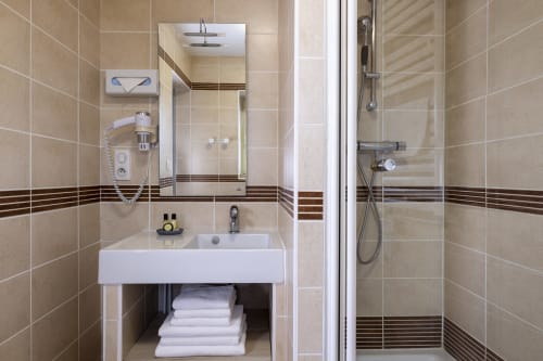 Salle de bain moderne aux carrelages beiges, lavabo blanc, miroir et douche à l'italienne à l'Hôtel De Lion Sur Mer