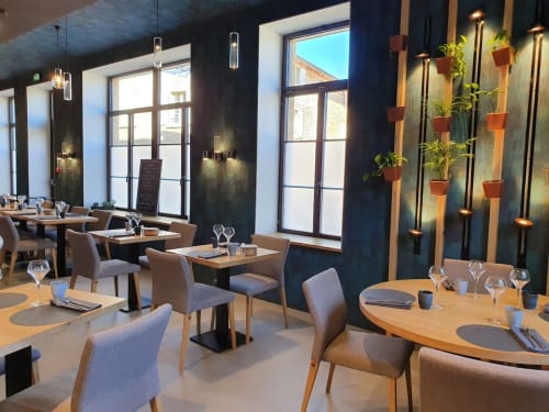Salle à manger moderne aux Terrasses Dorées : tables en bois, chaises beige, murs foncés, plantes suspendues et grandes fenêtres
